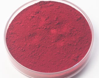 May include: A clear, circular petri dish containing a vivid, deep red powder. The powder has a fine, textured appearance, filling the dish. The dish is set against a plain white background.
