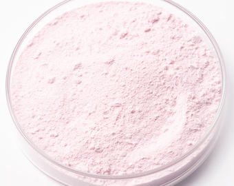 Può includere: Un piatto rotondo di vetro trasparente riempito con una polvere rosa chiaro. La polvere ha una consistenza fine e granulosa e riempie il piatto. Il piatto è posto su uno sfondo bianco, evidenziando il colore e la consistenza della polvere.