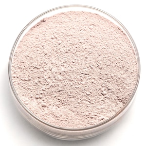 Peut inclure: Une boîte de Pétri en verre transparent remplie d'une poudre rose clair. La poudre a une texture fine et granulaire et semble être uniformément répartie dans la boîte. La boîte est posée sur un fond blanc.