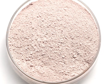 Può includere: Una capsula di Petri in vetro trasparente riempita con una polvere rosa chiaro. La polvere ha una consistenza fine e granulare e sembra essere distribuita uniformemente all'interno della capsula. La capsula è posta su uno sfondo bianco brillante.