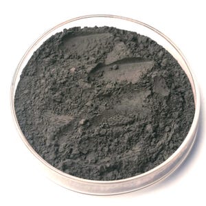 May include: A clear, round petri dish filled with a dark gray powder. The powder has a fine, textured appearance and fills the dish to the top. The dish is set against a white background.