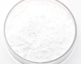 Pode incluir: Um prato redondo de vidro transparente preenchido com um pó branco fino. O pó tem uma aparência ligeiramente texturizada, e o prato está sobre um fundo branco brilhante. A impressão geral é limpa e estéril.