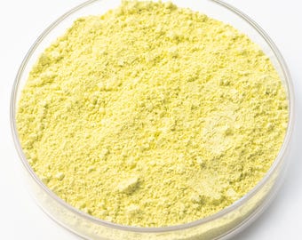 May include: A clear, round petri dish filled with a fine, yellow powder. The powder has a granular texture and fills the dish completely. The dish is set against a plain white background.