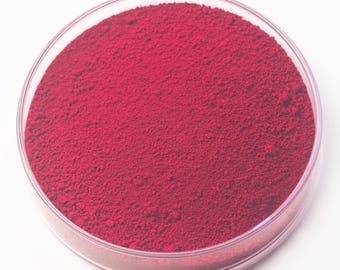 May include: A petri dish filled with a vibrant, deep red powder. The powder has a fine, granular texture and fills the clear, circular dish. The dish is set against a plain white background, highlighting the color and texture of the powder.