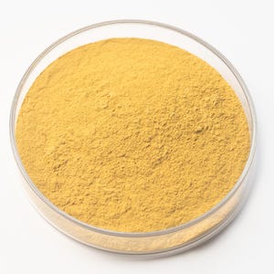 May include: A clear, round petri dish filled with a fine, yellow-brown powder. The powder has a uniform texture and fills the dish to the top. The dish is set against a plain white background.