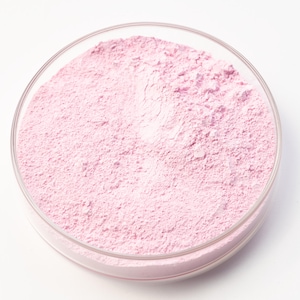 Può includere: Una capsula di Petri in vetro trasparente riempita con una polvere rosa chiaro. La polvere ha una consistenza fine e granulare e riempie la capsula. La capsula è posta su uno sfondo bianco.