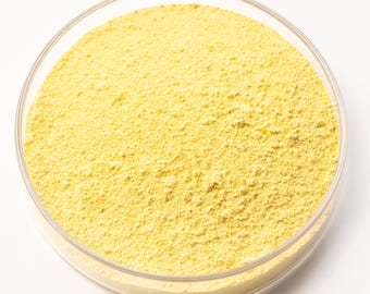 May include: A clear glass petri dish filled with a yellow powder. The powder has a fine, granular texture and is evenly distributed within the dish. The dish is set against a white background.