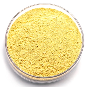 May include: A transparent glass bowl containing yellow powder. The powder has a fine, granular consistency and is uniformly spread within the bowl. The bowl is set against a white backdrop, accentuating the colour and texture of the powder.