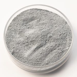 Può includere: Una capsula di Petri rotonda e trasparente riempita con una polvere fine e grigia. La polvere ha una superficie leggermente strutturata e sembra essere distribuita uniformemente all'interno della capsula. Il tutto è su uno sfondo bianco.