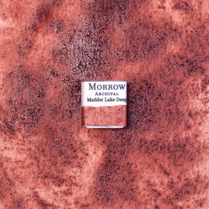 Close-up image of a half pan of Madder Lake Deep handmade watercolor paint, featuring a rich crimson hue with soft violet undertones and a translucent, matte finish. The pan rests on a neutral background, highlighting the pigment’s botanical origin and artisanal, small-batch craftsmanship. Ideal for artists seeking a historically accurate, plant-based red with elegance and warmth.