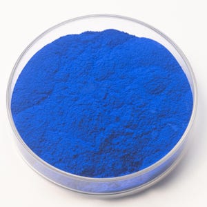 May include: A clear, round petri dish filled with a vibrant, finely ground blue powder. The powder has a smooth, even texture and fills the dish completely. The dish is set against a plain white background.