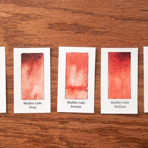 five watercolor paintings with different shades of orange, arranged on a wooden surface.
