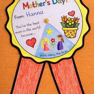Könnte beinhalten: Eine handgemachte Muttertagskarte mit einem gelb-schwarzen Zickzackrand, roten Bändern und dem Text "Happy Mother's Day!". Die Karte enthält eine Zeichnung von zwei Mädchen, Blumen und einem Herzen. Der Text lautet "From: Hanna" und "You're the best mom in the world because..."
