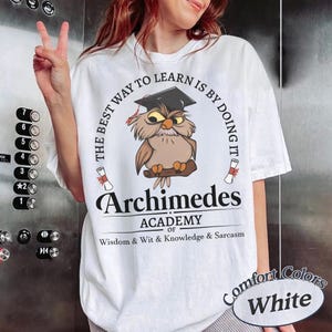 May include: A white t-shirt featuring a graphic of a brown owl wearing a black graduation cap. The text reads: THE BEST WAY TO LEARN IS BY DOING IT, Archimedes ACADEMY OF WISDOM & WIT & KNOWLEDGE & SARCASM. Two small diploma scrolls are included.
