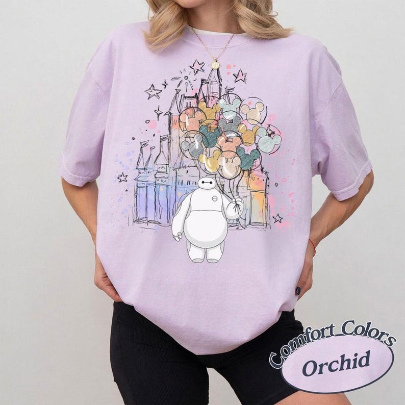 Puede incluir: Camiseta color orqu&iacute;dea con un gr&aacute;fico de Baymax sosteniendo globos de Mickey Mouse frente a un castillo. El dise&ntilde;o incluye estrellas y detalles de estilo acuarela. La camiseta tiene mangas cortas y un corte holgado.