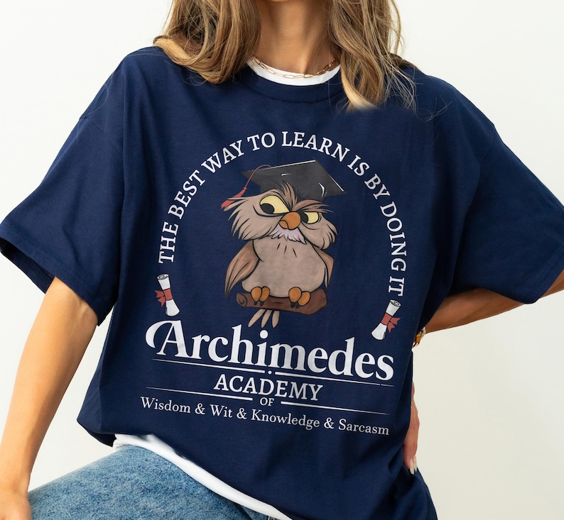 May include: A navy blue t-shirt featuring a graphic of an owl wearing a graduation cap, perched on a branch. The text reads: THE BEST WAY TO LEARN IS BY DOING IT, Archimedes ACADEMY OF Wisdom & Wit & Knowledge & Sarcasm, with two diploma scrolls.