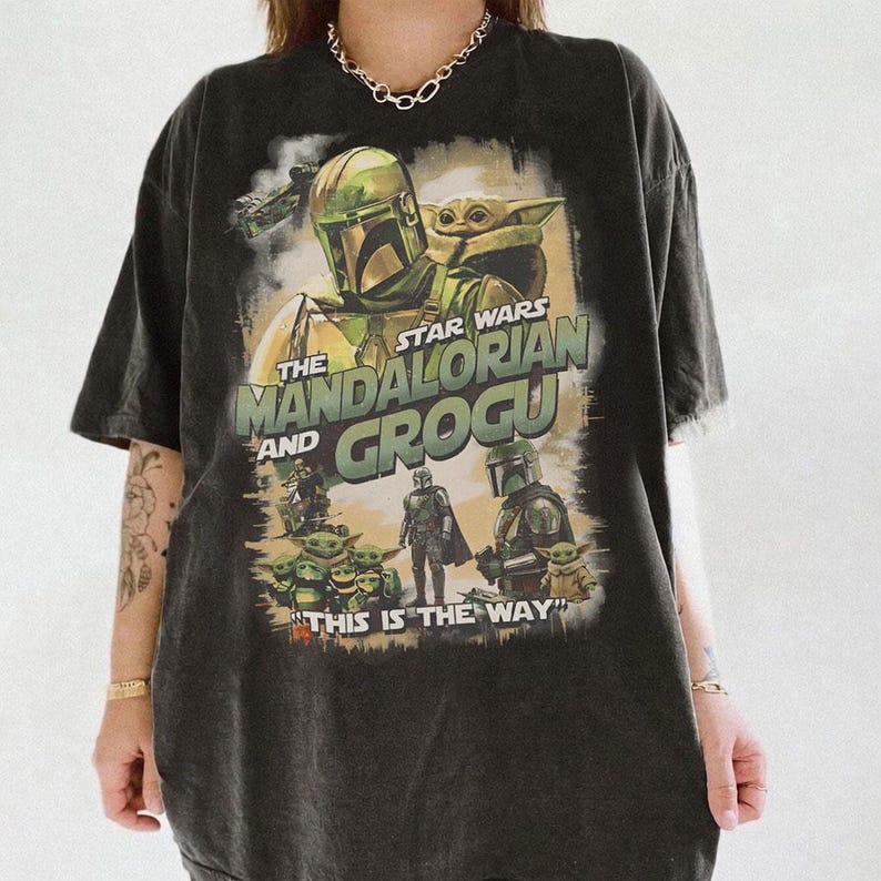 Może przedstawiać: Ciemnoszara koszulka z grafiką Star Wars z The Mandalorian i Grogu. Projekt zawiera obrazy Mandalorianina, Grogu i innych postaci, z napisem "THIS IS THE WAY" na dole.