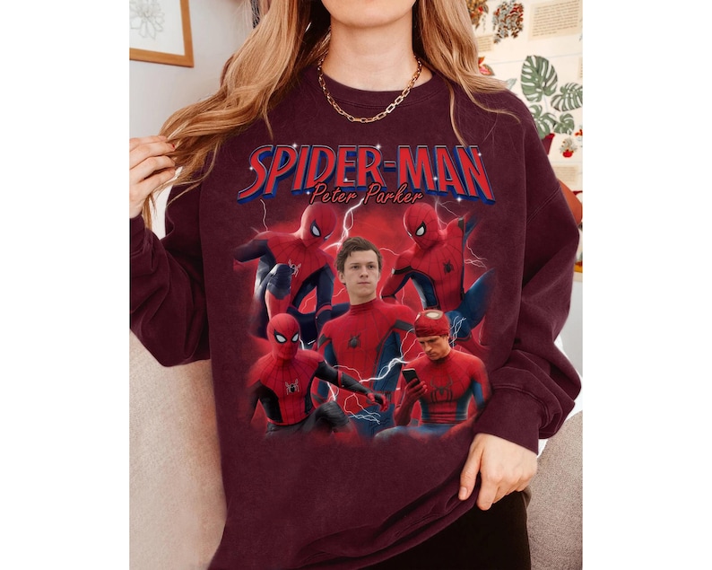 Może przedstawiać: Bordowa bluza z grafiką Spider-Mana i napisem "Spider-Man Peter Parker" w kolorze czerwonym i niebieskim. Projekt zawiera wiele zdjęć Spider-Mana w pozach akcji, ze zdjęciem aktora w centrum.