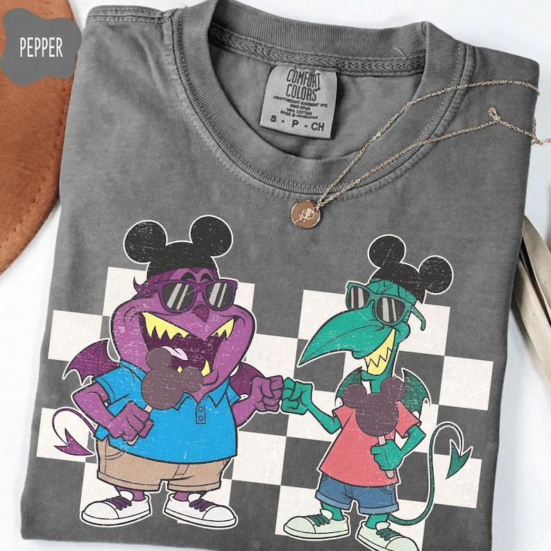 May include: A gray Comfort Colors t-shirt featuring a cartoon graphic of two monster-like characters wearing sunglasses and holding ice cream bars. The shirt has a checkerboard pattern in the background and a gold necklace.