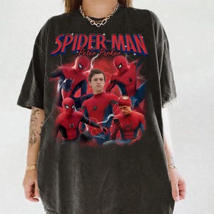 Może przedstawiać: Ciemnoszara koszulka z grafiką Spider-Mana w r&oacute;żnych pozach, z napisem "SPIDER-MAN Peter Parker" w kolorze czerwonym i niebieskim. Projekt zawiera błyskawice i wiele wizerunk&oacute;w superbohatera.