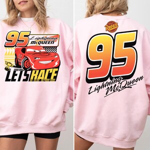May include: A light pink sweatshirt featuring Lightning McQueen from the Cars movie. The front graphic includes the number 95, the character's name, and the phrase "Let's Race." The back displays a large number 95 and the character's name.