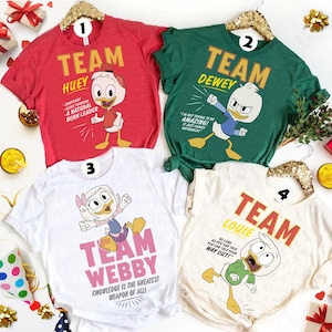 Puede incluir: Cuatro camisetas de manga corta con personajes de patos de dibujos animados. La roja dice TEAM HUEY, la verde TEAM DEWEY, la blanca TEAM WEBBY y la crema TEAM LOUIE, cada una con texto específico para cada personaje.