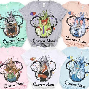 May include: Six short-sleeved t-shirts in mint, heather grey, peach, light pink, white, and light blue. Each shirt features a black hand-drawn Mickey Mouse ear outline framing a cartoon character, a castle, balloons, and the text Custom Name.