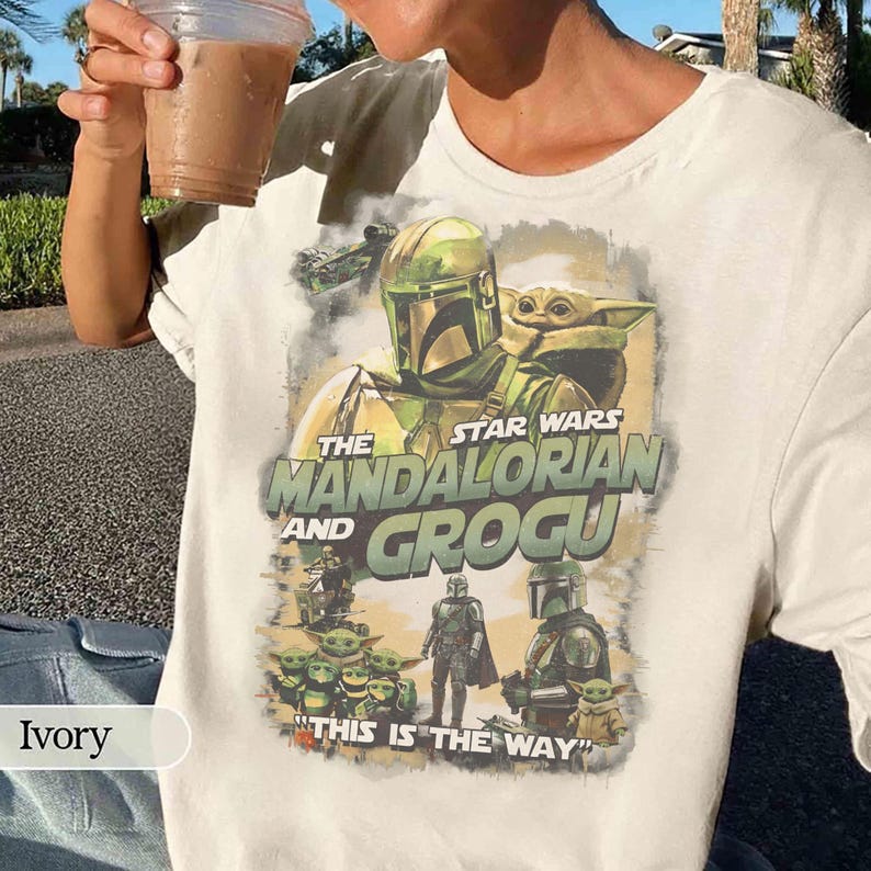 Może przedstawiać: Kremowa koszulka z motywem Star Wars. Grafika zawiera napis "The Mandalorian and Grogu" oraz wizerunki postaci. Na koszulce znajduje się r&oacute;wnież fraza "This is the Way".