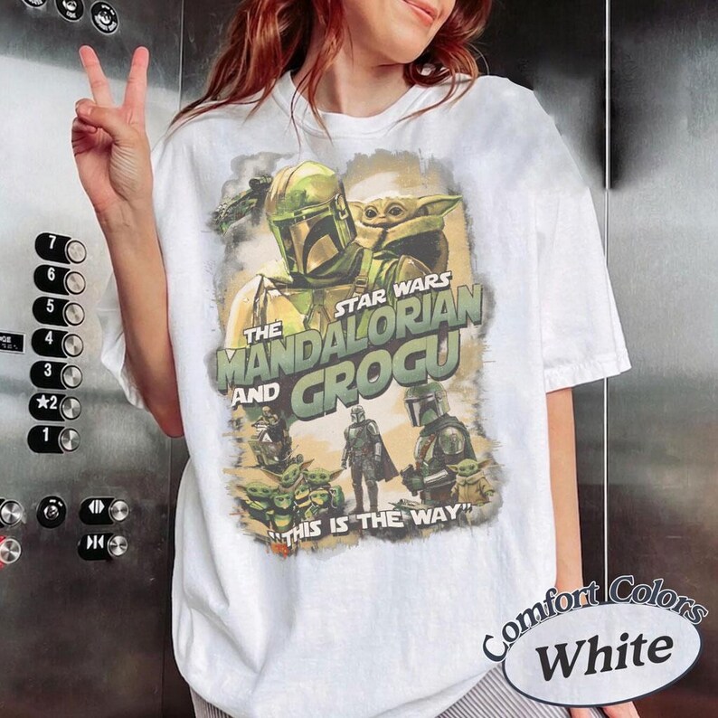 Może przedstawiać: Biała koszulka z motywem Star Wars z The Mandalorian i Grogu. Grafika zawiera wizerunki postaci i napis "THIS IS THE WAY". Koszulka jest oznaczona jako "Comfort Colors White".