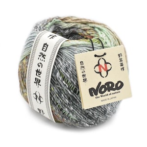 Op de afbeelding: Een bol Noro-garen in grijstinten, groen en bruin. Het garen is verpakt met een wit etiket met Japanse tekst en een label met het Noro-logo en de tekst "Made in Japan". Het garen is voor brei- en haakprojecten.