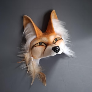 Peut inclure: Un masque de renard artisanal avec de la fourrure orange, blanche et beige. Le masque présente des yeux détaillés, un nez noir et des plumes décoratives. Le masque de renard est une pièce de costume unique.