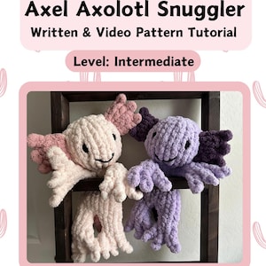 Könnte beinhalten: Zwei gehäkelte Axolotl-Plüschtiere, eines rosa und eines lila, sitzen auf einem Holzregal. Die Plüschtiere haben Glitz Augen und sind aus einem strukturierten Garn gefertigt. Das Bild trägt den Titel "Axel Axolotl Snuggler" und "Written & Video Pattern Tutorial". Der Text "Level: Intermediate" ist ebenfalls im Bild enthalten.