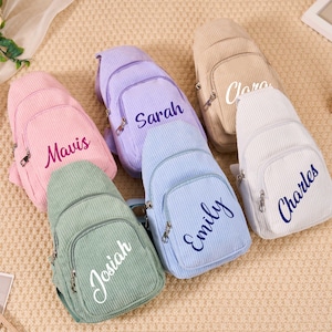 Könnte beinhalten: Eine Auswahl an Cord-Umhängetaschen in Pastelltönen: Rosa, Lavendel, Hellblau, Beige und Weiß. Jede Tasche hat eine Vordertasche und einen Namen, der in einer Kontrastfarbe gestickt ist. Diese Taschen sind für den täglichen Gebrauch geeignet.