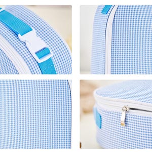 Puede incluir: Una bolsa azul y blanca con estampado de cuadros vichy con cremallera blanca y correa azul con hebilla blanca. La bolsa tiene forma redondeada y ribete blanco.