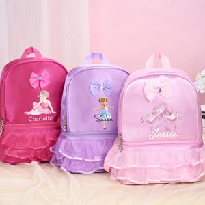 May include: Three ballet-themed backpacks in pink, purple, and lavender. Each backpack features a bow, a ballerina graphic, and a name. The pink backpack has a tutu-style skirt and the name "Charlotte". The purple backpack has the name "Susan". The lavender backpack has the name "Jessie".
