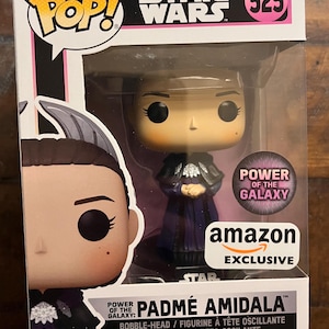 May include: A Funko Pop Star Wars figure number 525 of Padmé Amidala from the Power of the Galaxy collection. The vinyl bobble-head is inside a display box with an Amazon Exclusive sticker, featuring a purple outfit and detailed facial features.