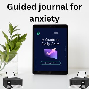 May include: A digital tablet displays the text "A Guide to Daily Calm" with a purple graphic and the handle "@reallygreatsite." The words "Guided journal for anxiety" are at the top. Two black printers and a vase of green leaves are also in the image.