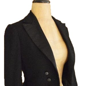 Puede incluir: Chaqueta de esmoquin negra con solapa de muesca y tres botones. La chaqueta se exhibe en un maniqu&iacute;. La chaqueta a medida tiene un dise&ntilde;o cl&aacute;sico, adecuado para eventos formales. La tela de la chaqueta parece ser un material liso y oscuro.