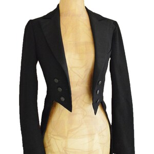 Puede incluir: Chaqueta levita negra sobre maniqu&iacute;. Presenta solapa de muesca, tres botones a cada lado y cola dividida. La tela es oscura y lisa. Prenda cl&aacute;sica de vestir formal.