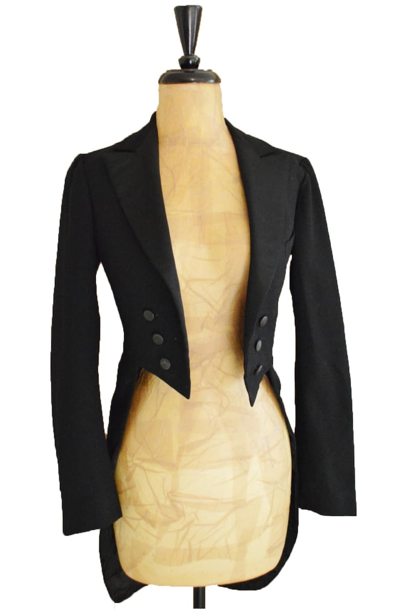 Puede incluir: Chaqueta levita negra sobre maniqu&iacute;. Presenta solapa de muesca, tres botones a cada lado y cola dividida. La tela es oscura y lisa. Prenda cl&aacute;sica de vestir formal.