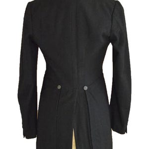 Puede incluir: Un frac negro formal exhibido en un maniqu&iacute;. El abrigo presenta mangas largas, solapas y una espalda dividida. Se ven dos botones en la parte trasera. El abrigo est&aacute; hecho de una tela oscura y lisa.