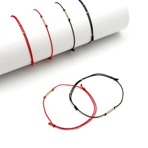 May include: A collection of adjustable cord bracelets in red and black, featuring small gold-toned metallic beads. Some bracelets have single beads while others feature a row of five beads. The cords are thin and finished with sliding knots.