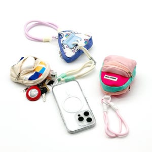 May include: An assortment of small pouches and accessories, including a clear phone case, a small backpack-shaped pouch, and a coin purse. The pouches are in various colors, including pink, blue, and white, and are connected to lanyards.