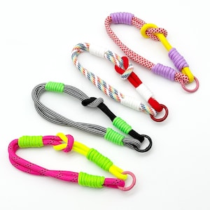 May include: Four colorful rope dog toys in various patterns and colors, including pink, black and white, and rainbow. Each toy features a knot and a metal ring. The toys are designed for pets.