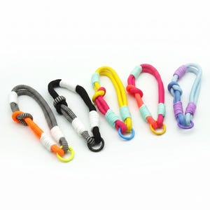 May include: A collection of colorful rope leashes in various designs. Each leash features a loop, a knot, and a metal or plastic ring. The color palette includes black and white, orange, yellow, pink, blue, and purple, with accents of turquoise.