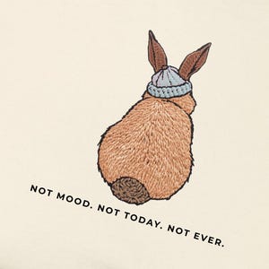 May include: Cream-coloured t-shirt with an embroidered illustration of a brown rabbit wearing a light blue beanie. The text "NOT MOOD. NOT TODAY. NOT EVER." is printed in black below the rabbit. The shirt is made of a soft material.