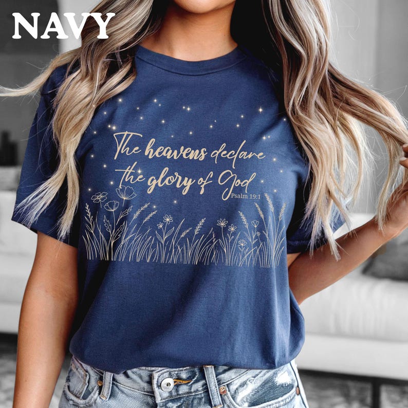 An espresso brown t-shirt with a gold starry sky and wildflower illustration, folded on a white surface next to a hat.