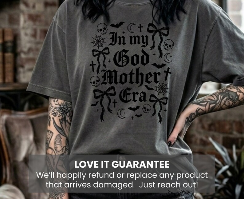 A person wearing a dark gray t-shirt with the same black In my God Mother Era gothic graphic design.