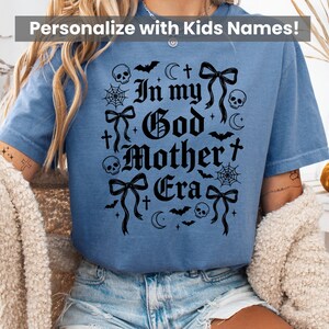 A person wearing a blue t-shirt featuring the In my God Mother Era gothic graphic in black.
