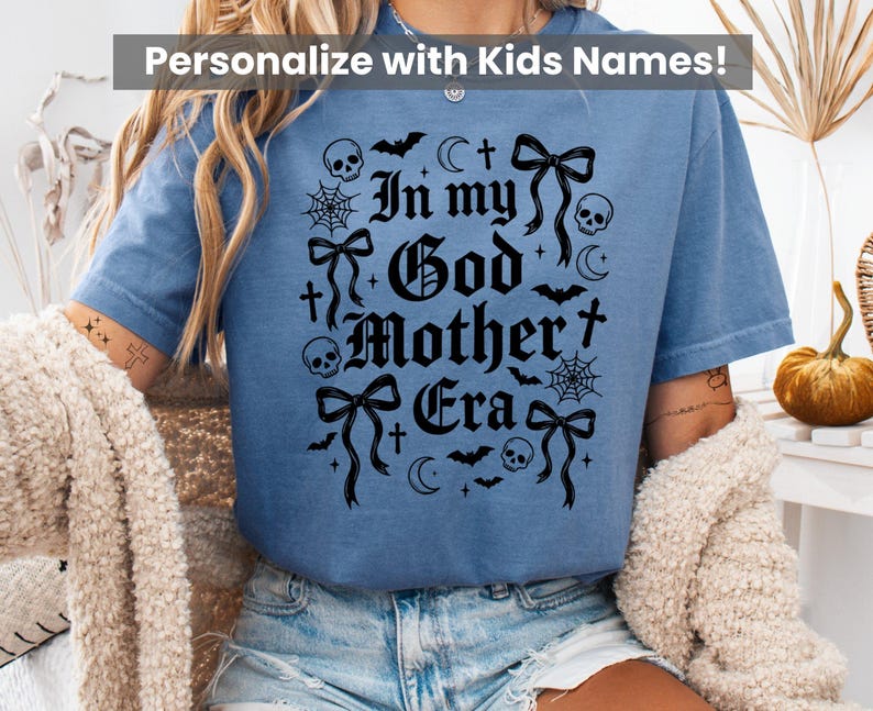 A person wearing a blue t-shirt featuring the In my God Mother Era gothic graphic in black.